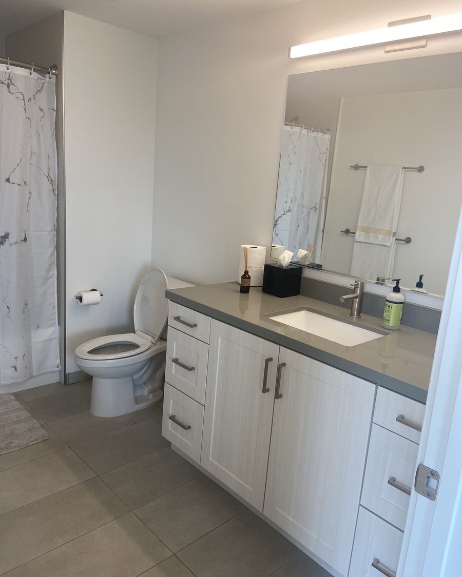 Short-term rental bathroom after a turnover clean: vanity cleared, mirror and fixtures polished, fresh towels hung squared on the rail, tile floor mopped.